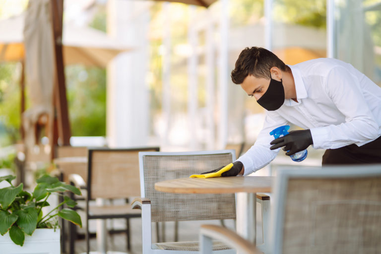 Young Waiter in protective face mask and gloves sanitizing surfa