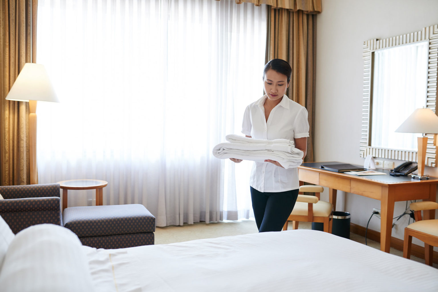 A female hotel maid brings towels into a hotel room