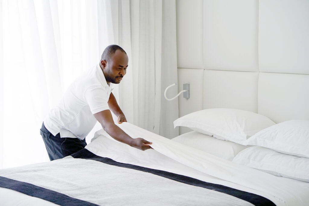 Housekeeper making bed in hotel room.